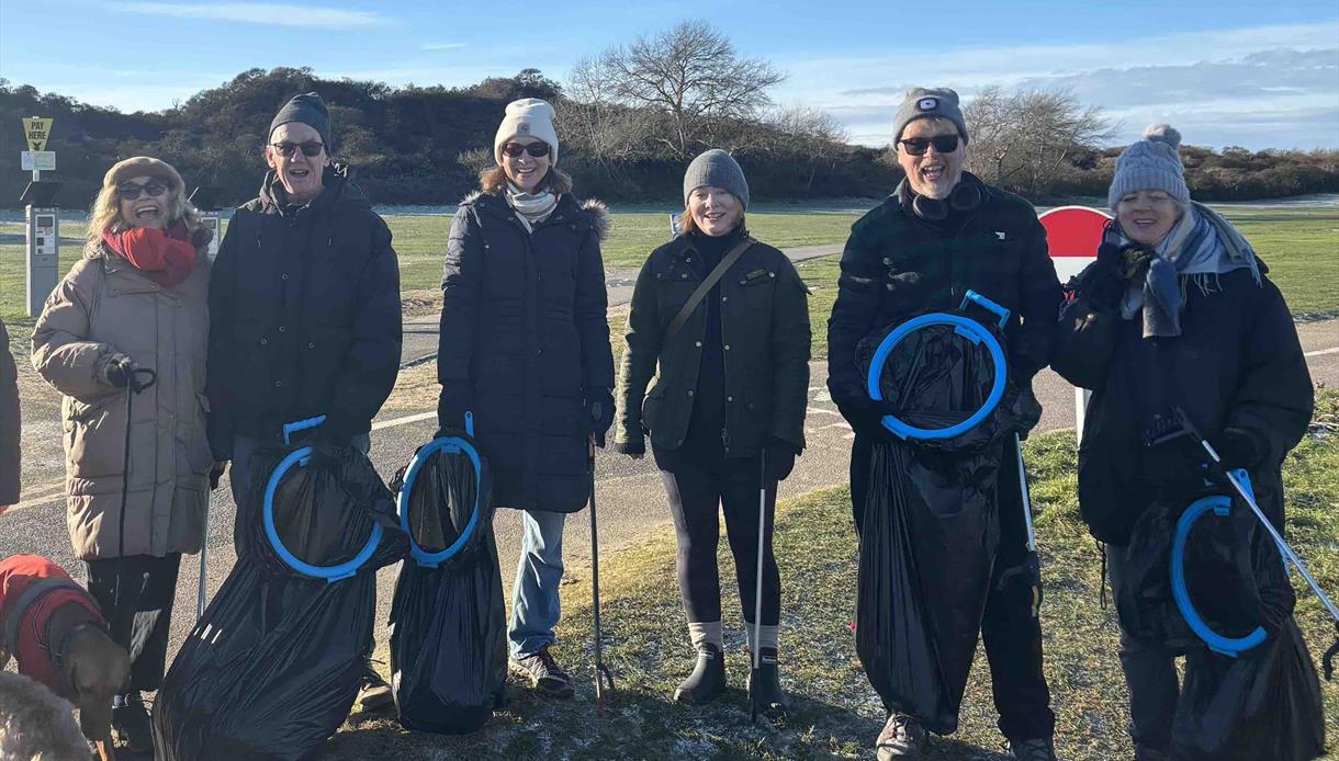 Volunteers at a community beach clean in Camber, standing outdoors with litter pickers and full rubbish bags on a sunny day.