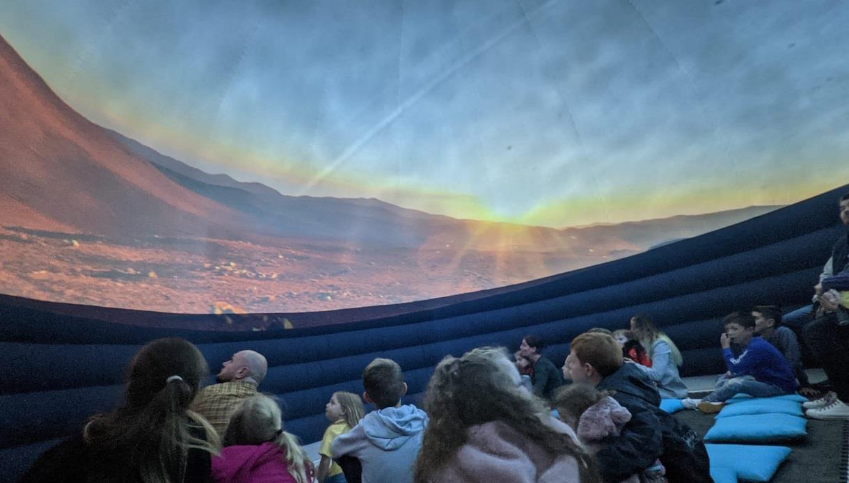image shows the planetarium at Hastings museum. It also shows a picture of the sky with children and adults sitting and looking up.