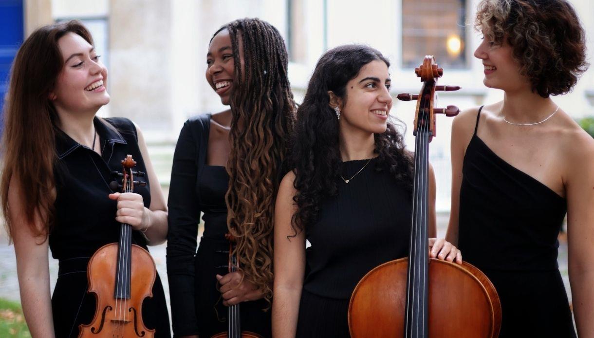 Four musicians in black attire holding string instruments, standing outdoors for a Spring Quartet concert.