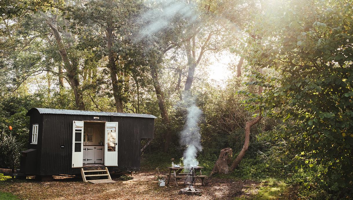 Photograph of a black glamping hut in a woods with smoking fire.