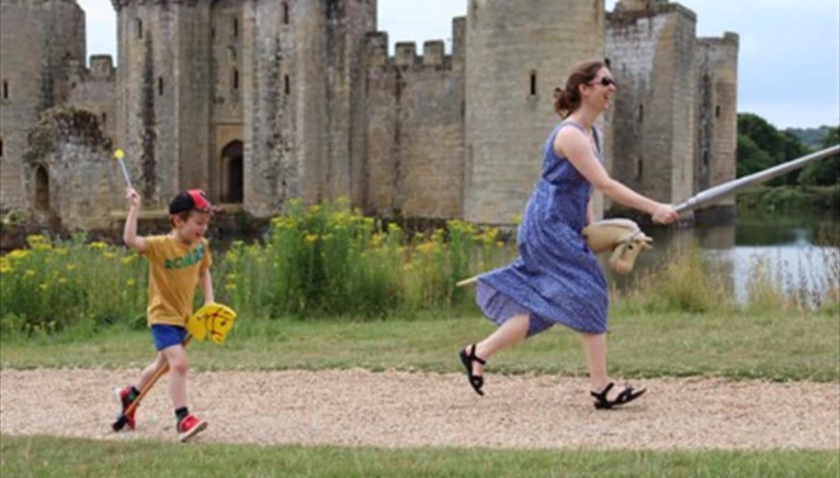 Summer of Play at Bodiam Castle, with visitors running on hobby horses beside the medieval castle and moat.