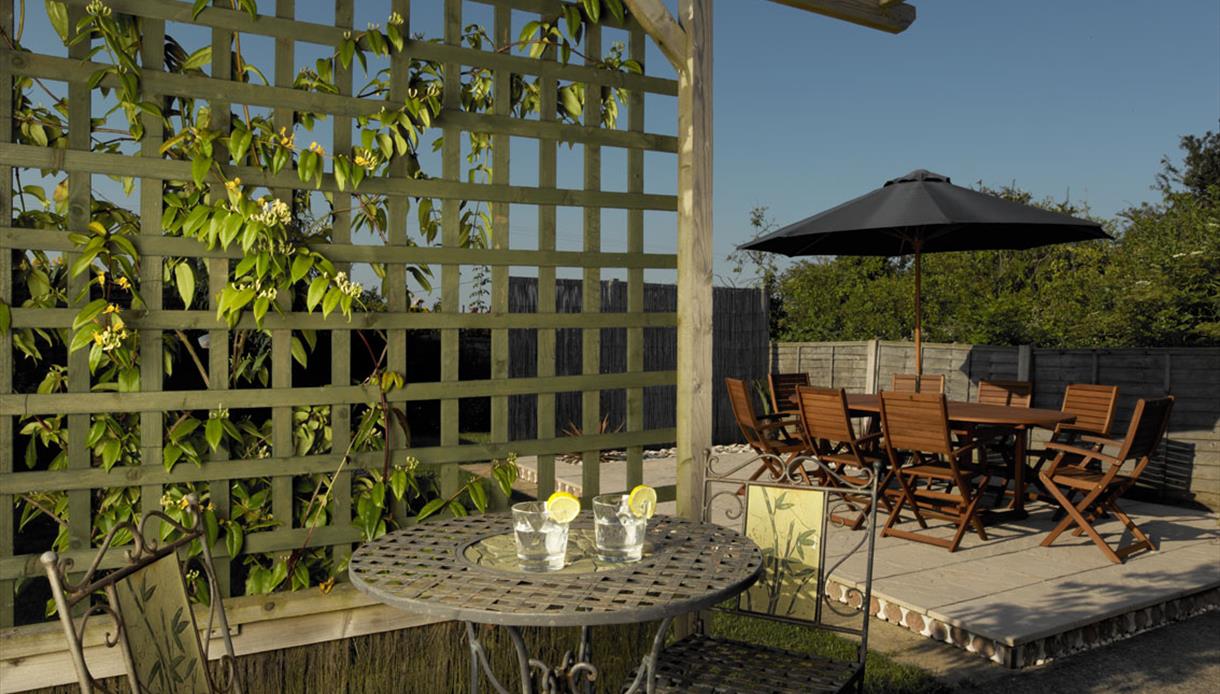 Garden at Stoats Holiday Home shows terrace and tables in sunshine