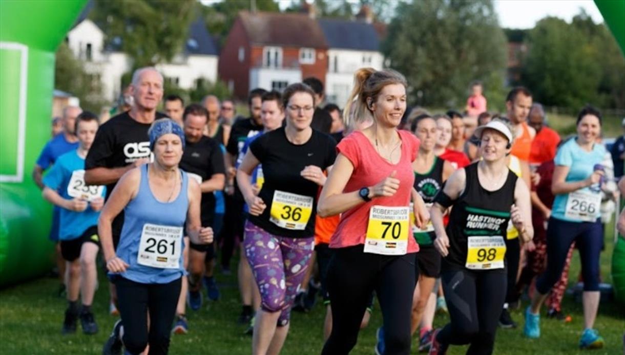 Group of runners wearing numbered bibs start a race for Nice Work.