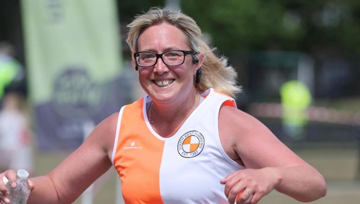 Runner in an orange and white athletic top holding a water bottle during an outdoor race.