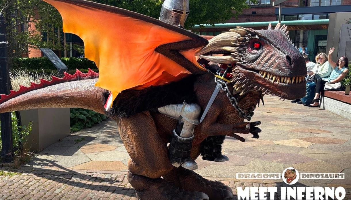 Large dragon costume with orange wings and glowing red eyes entertains visitors at priory meadow shopping.