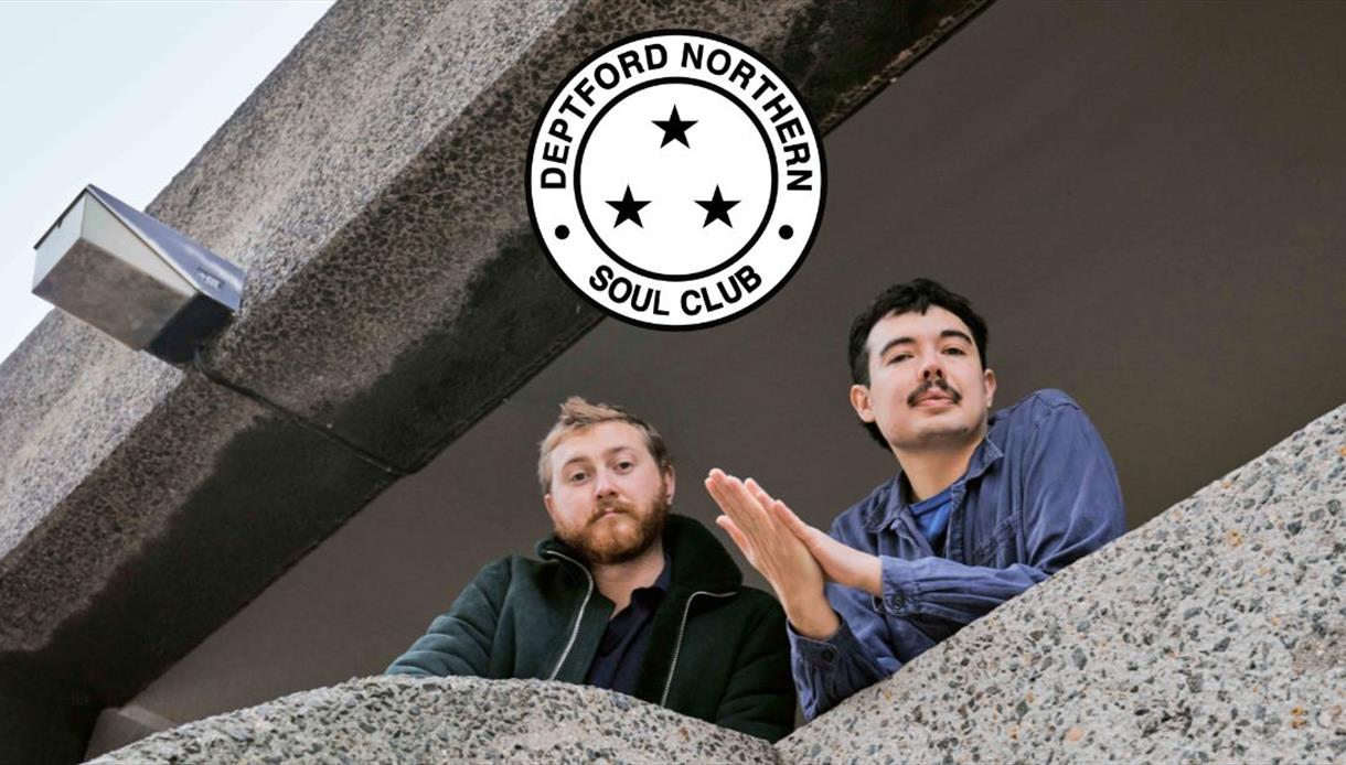 Two people stand on a concrete balcony beneath a ‘Deptford Northern Soul Club’ logo.