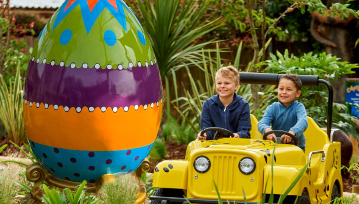 Two children in a yellow jeep ride next to a large colourful egg at Drusillas Park.