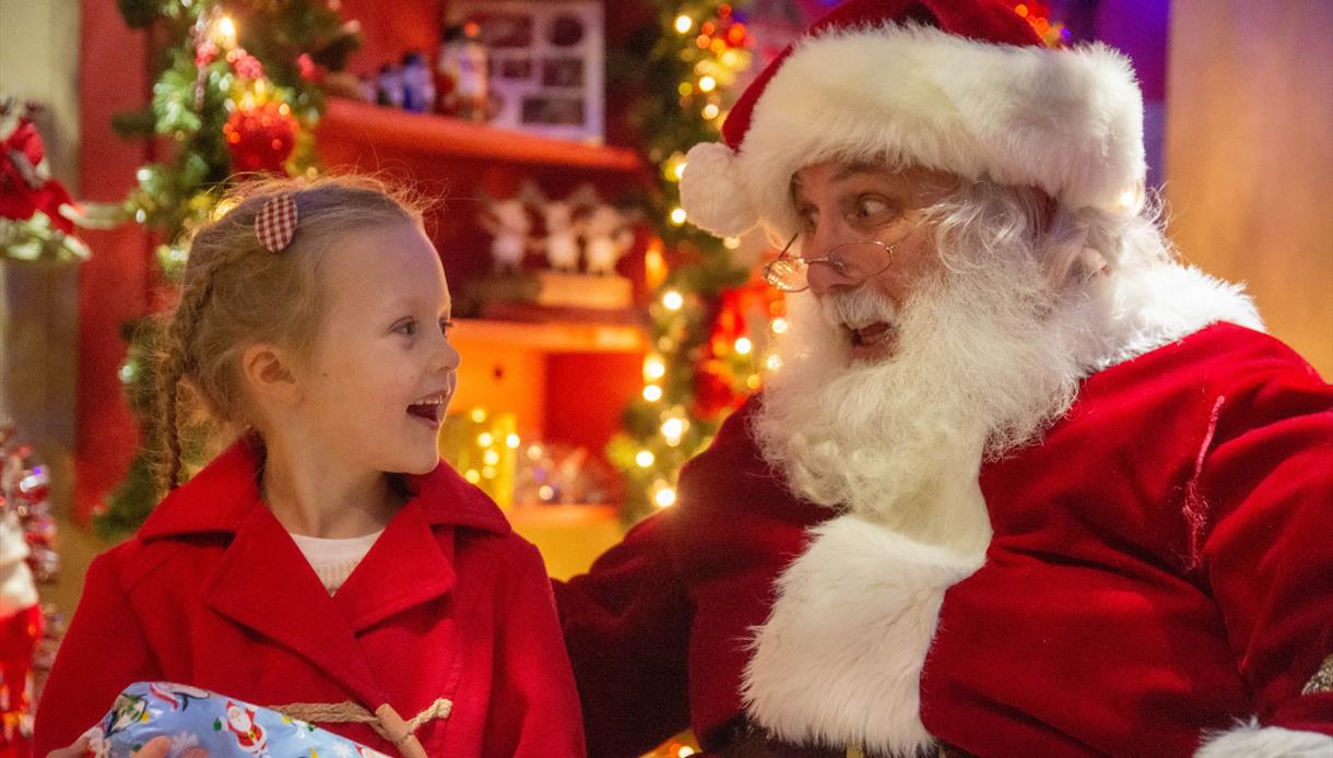 A young girl and Father Christmas look at each other engaged in conversation.