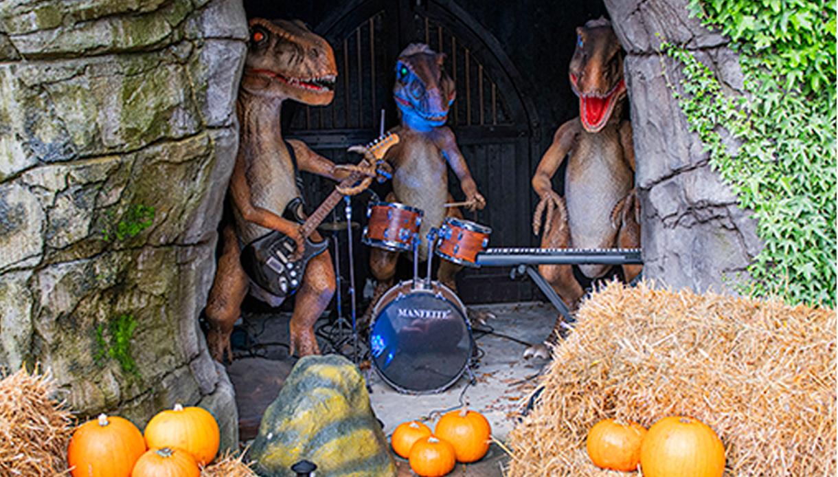 Halloween at Knockhatch Adventure Park featuring animatronic dinosaurs playing instruments among pumpkins and hay bales.