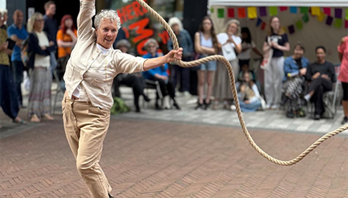 Outdoor performance by JUTE at De La Warr Pavilion, showing an older dancer swinging a rope as an audience watches.