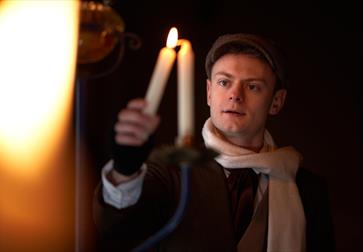a young man wearing a cap and scarf lighting a candle.