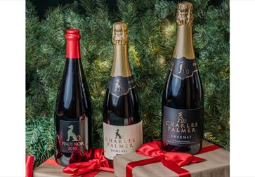 Three Charles Palmer wine bottles with festive ribbons in front of a green Christmas tree background.