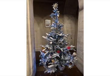 Decorated Christmas tree with silver tinsel, ornaments, and lights in a stone archway.