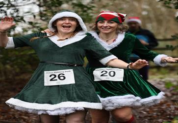 Festive holiday run: two women dressed as Santa jogging together on a forest path.