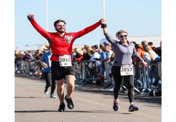 Focused runners mid-stride during an outdoor street race, urban backdrop with barriers and onlookers.