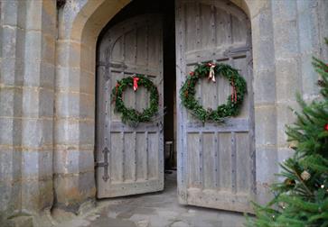 image shows two doors at bodiam castle with christmas wreaths on. In the corner of the image, you can see part of a christmas tree with red baubles on