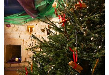 image shows a festive christmas tree inside Bodiam castle. On the tree are cinnamon sticks, lights and decorations