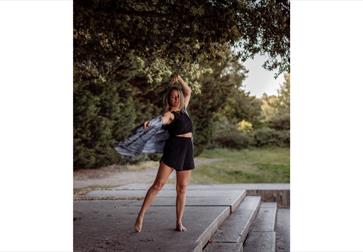 A woman is outdoors on a patio area moving her body. Her clothes flow in the movement.