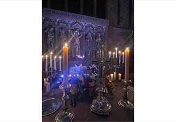 Image shows the Altar at St Thomas the Martyr Church with tall candles that are alight and an image of Jesus in the background on the cross.