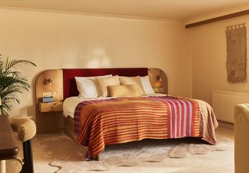Image shows the inside of one of the bedrooms at Crafted at Powdermills. The Room is bright, light and neutral tones. The bed is in the centre of the