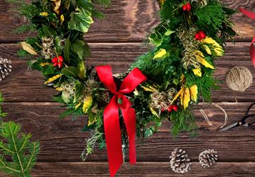Image shows a christmas wreath decorated with bows, holly and pine cones