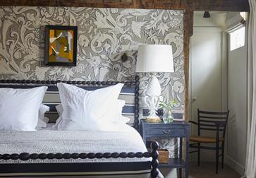 interior view of bedroom shows decorative wallpaper, wooden chair, and deluxe double bed with white sheets