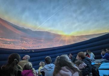 image shows the planetarium at Hastings museum. It also shows a picture of the sky with children and adults sitting and looking up.