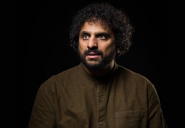 Nish Kumar on a black background wearing brown