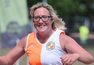 Runner in an orange and white athletic top holding a water bottle during an outdoor race.