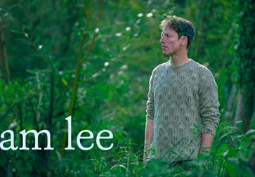 Image shows singer, Sam Lee, in a leafy, green outdoor environment with 'Sam Lee' written