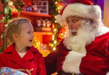 A young girl and Father Christmas look at each other engaged in conversation.