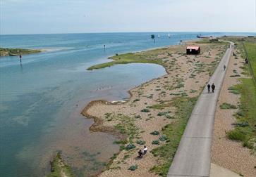 aerial view of a harbour, with grass and vegetation, single shore and a long tarmac path leading along the shoreline.