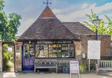 front external view of battle museum. A small brick building with pointed tiled roof with a weathervane on top.