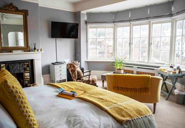 Bright yellow room at The Laindons with large windows overlooking Hastings rooftops and coastline.