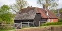 Traditional timber-clad outbuilding and cottage beside the mill pond at Bateman’s in East Sussex.