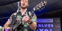 Jazz musician performing with guitar and microphone on stage at Rye Jazz Festival.