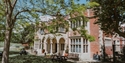 Exterior of Hastings Museum & Art Gallery, a red-brick building set in gardens with trees and picnic benches.