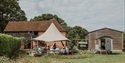 Oxney Organic Estate vineyard tour group gathered under a canopy beside historic farm buildings.