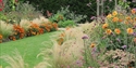 Colourful flower borders and ornamental grasses at Merriments Gardens, lining a winding lawn pathway.