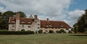 Michelham Priory's historic stone house set within expansive lawns under a dramatic sky.