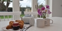 Breakfast table with croissants, tea and flowers inside a Rye & Beyond holiday cottage.