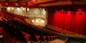 Interior of White Rock Theatre showing rows of red seats facing stage with closed red curtain.