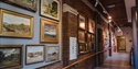 Wall of framed paintings inside Hastings Museum & Art Gallery along a bright corridor with track lighting.