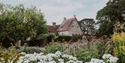 Michelham Priory surrounded by colourful flower beds and mature trees in the historic gardens.