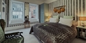 Stylish bedroom at The Laindons with striped wallpaper, bay windows, armchair and mirrored wardrobe.