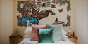 Cosy bedroom at Starcroft Farm Cabin with colourful cushions and a nature-inspired mural above the bed.
