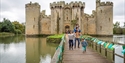 Family crossing the bridge to Bodiam Castle, with the moat and gatehouse in the background.