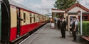 Kent & East Sussex Railway staff wave as a vintage passenger train departs a heritage station platform.