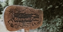 Wooden Starcroft Farm Cabins sign beside a tree-lined path, featuring hand-carved nature-inspired details.
