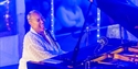 Emile Sande performing on stage beside a grand piano under blue lights at Rye Jazz Festival.
